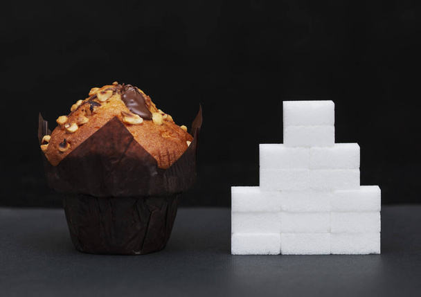 suikergehalte naast de cupcake, op elkaar gestapelde blokjes suiker, de hoeveelheid suiker in de schotel - Foto, afbeelding