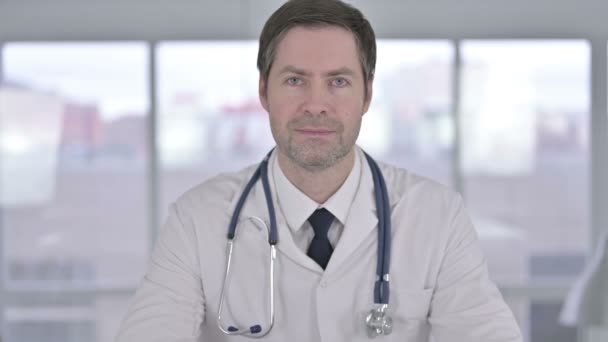 Portret uśmiechniętego lekarza w średnim wieku patrzącego w kamerę  - Materiał filmowy, wideo
