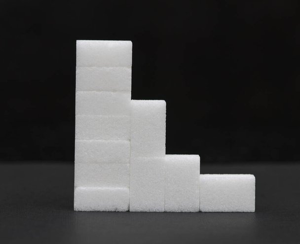fehér kockacukor egy piramisban, cukorszinttel, sötét háttérrel - Fotó, kép