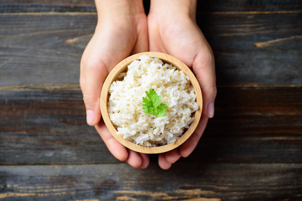 Hand hält Schüssel mit gekochtem Reis mit Quinoasamen auf Holzgrund, gesunde Ernährung, Draufsicht - Foto, Bild