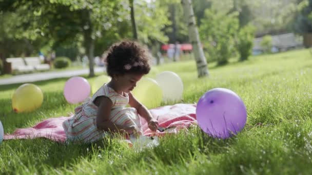 Little african-american girl is sitting in the park and drawing - Materiał filmowy, wideo