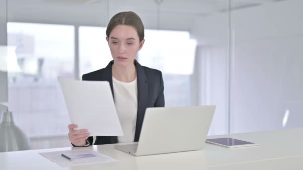 Трудолюбивая молодая предпринимательница читает документы в офисе - Кадры, видео