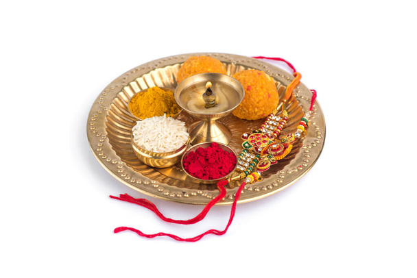 Indian Festival: Rakhi with rice grains, kumkum, sweets and diya on plate with an elegant Rakhi. A traditional Indian wrist band which is a symbol of love between Brothers and Sisters - Photo, image