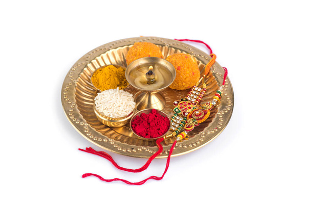 Indian Festival: Rakhi with rice grains, kumkum, sweets and diya on plate with an elegant Rakhi. A traditional Indian wrist band which is a symbol of love between Brothers and Sisters - Photo, image