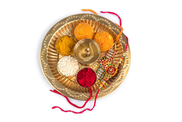 Indian Festival: Rakhi z ziarnami ryżu, kumkum, słodycze i diya na talerzu z eleganckim Rakhi. Tradycyjna indyjska opaska na nadgarstek, która jest symbolem miłości między braćmi i siostrami - Zdjęcie, obraz