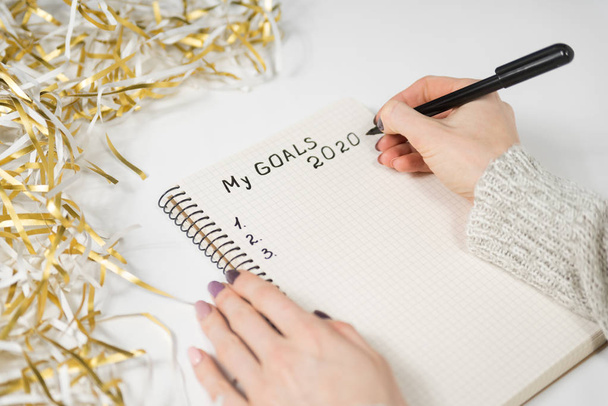 Female hands writing My Goals 2020 in a notebook. Tinsel, New Years concept - Фото, зображення