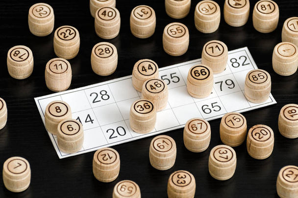 Barriles de lotería de madera y carta para jugar en una mesa negra
 - Foto, imagen