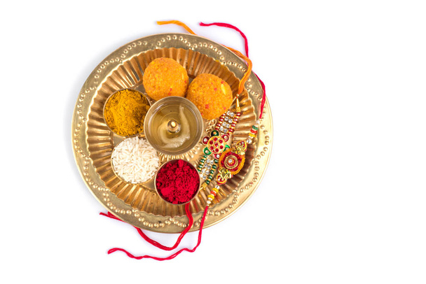 Indian Festival: Rakhi with rice grains, kumkum, sweets and diya on plate with an elegant Rakhi. A traditional Indian wrist band which is a symbol of love between Brothers and Sisters - Φωτογραφία, εικόνα