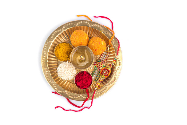 Indian Festival: Rakhi with rice grains, kumkum, sweets and diya on plate with an elegant Rakhi. A traditional Indian wrist band which is a symbol of love between Brothers and Sisters - Foto, imagen