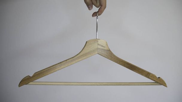 Cintre à vêtements en bois suspendu à un doigt féminin sur un fond gris
. - Photo, image
