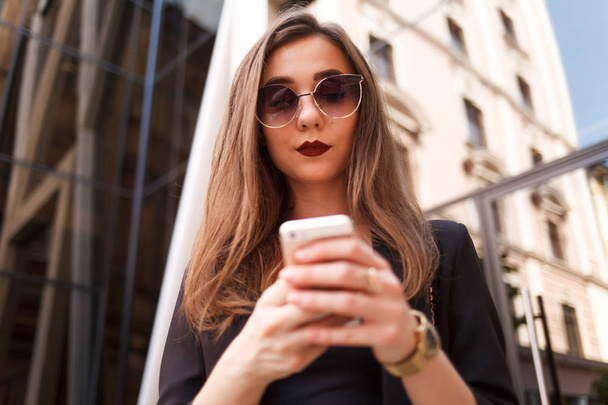 cute young girl in sunglasses uses a smartphone. stylish lady uses a smartphone for communication - Foto, Imagen
