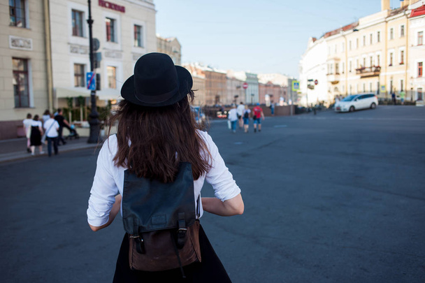 Young woman in hat walking in city, back view. Girl tourist enjoys the walk. - Photo, image