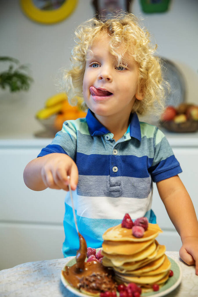 Little curly boy eating sweet pancakes - Fotografie, Obrázek