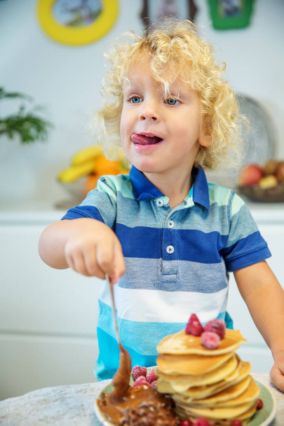 Little curly boy eating sweet pancakes - Φωτογραφία, εικόνα