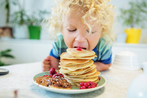 Little curly boy eating sweet pancakes - Fotografie, Obrázek