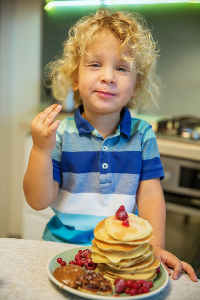 Little curly boy eating sweet pancakes - Foto, afbeelding
