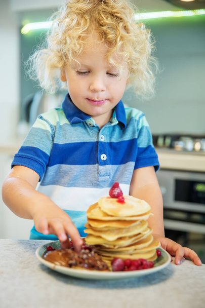 Little curly boy eating sweet pancakes - Фото, зображення