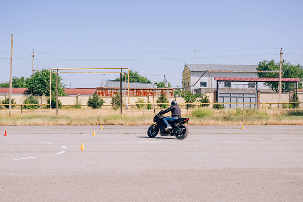 Alusta opettelee ajamaan moottoripyörää. Moottoripyöräkoulun oppitunteja. Pyöräilykursseja aikuisille. Mies oppii ajamaan pyörällä. Parannetaan ajotaitoa koulutuskentällä
 - Valokuva, kuva