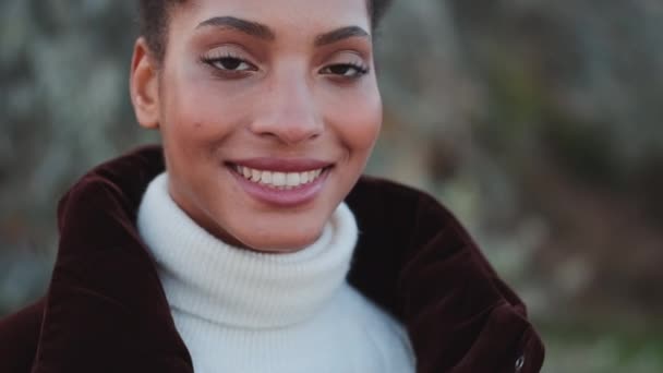 Close up shot of smiling African American girl in down jacket happily looking in camera outdoor - Felvétel, videó