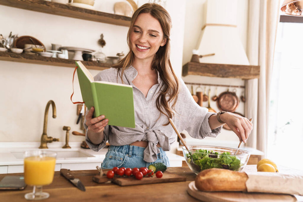 Pretty lady indoors at the kitchen cooking holding notebook. - Photo, Image