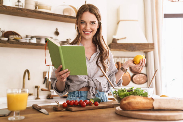 Woman indoors at the kitchen cooking holding notebook and lemon. - Foto, Imagen