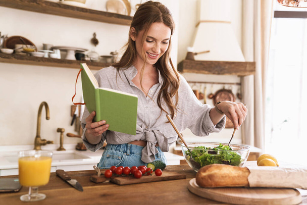 Pretty lady indoors at the kitchen cooking holding notebook. - Φωτογραφία, εικόνα