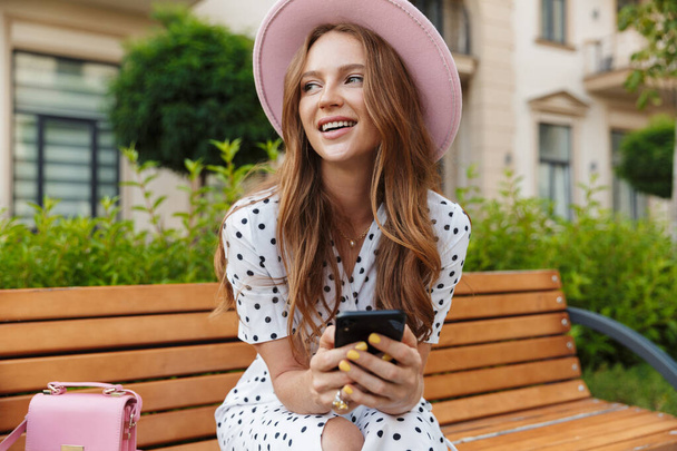 Smiling young redhead woman using mobile phone. - Foto, afbeelding