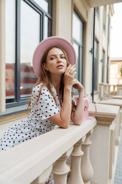 Young redhead woman on a porch outdoors in dress and hat. - Foto, afbeelding