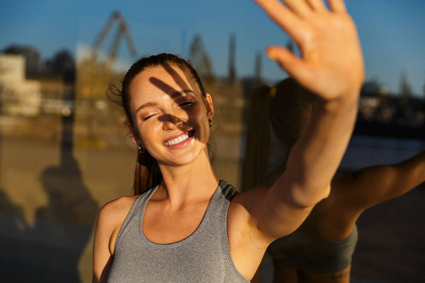 Smiling fit young sportsgirl standing at a glass wall building outdoors - Foto, Bild
