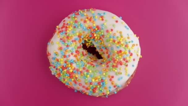 Delicious sweet donut rotating at pink background. Top view of colorful doughnut - Filmati, video
