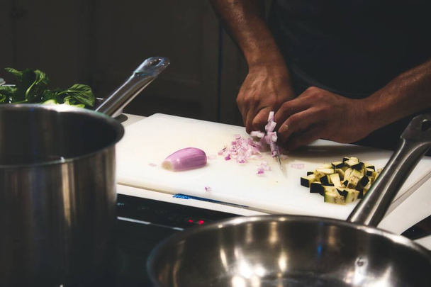 Nahaufnahme von Menschenhänden, die Zwiebeln auf einem Schneidebrett in einer professionellen Küche schneiden - Foto, Bild