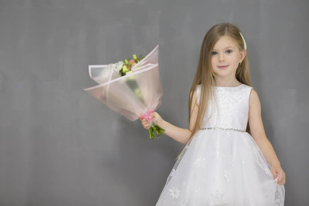 Kaunis pieni tyttö lapsi kukkakimpun kanssa harmaalla taustalla
 - Valokuva, kuva