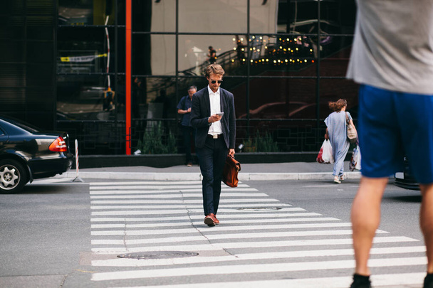Atrakcyjny biznesmen z telefonem komórkowym pędzi do pracy przechodząc przez ulicę - Zdjęcie, obraz