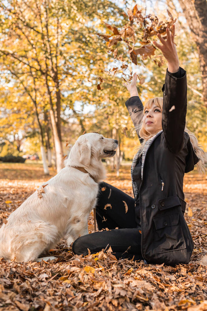 χαρούμενη ιδιοκτήτρια γυναίκα παίζει με το σκύλο της στο πάρκο του φθινοπώρου - Φωτογραφία, εικόνα