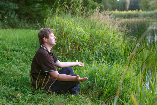 Молодий красивий чоловік сидить біля лісового озера і розслабляється
 - Фото, зображення