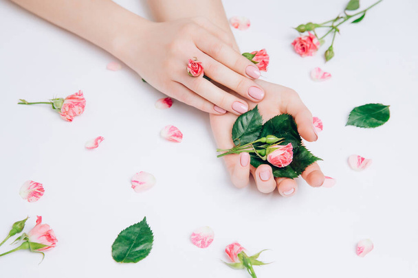 Detailní záběr krásné sofistikované ženské ruce s růžovými květy na bílém pozadí. Koncepce péče o ruce, krém, lázně. - Fotografie, Obrázek