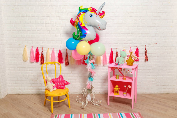 Balloons in the form of a unicorn. Idea for decorating unicorn style first year birthday party. Paper garlands on a white brick wall and photo booth props. Unicorn decoration for festival party for girl. - 写真・画像