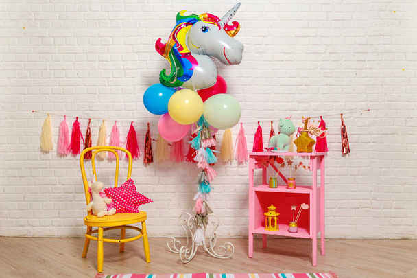 Balloons in the form of a unicorn. Idea for decorating unicorn style first year birthday party. Paper garlands on a white brick wall and photo booth props. Unicorn decoration for festival party for girl. - Фото, изображение