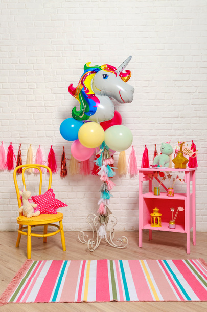 Balloons in the form of a unicorn. Idea for decorating unicorn style first year birthday party. Paper garlands on a white brick wall and photo booth props. Unicorn decoration for festival party for girl. - 写真・画像