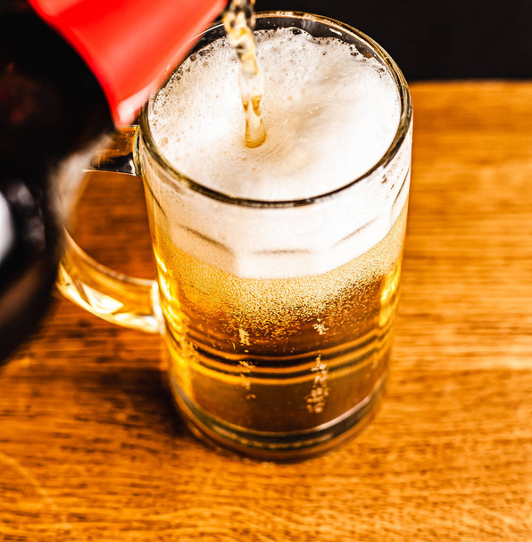 Cerveza fría con espuma en una taza, sobre una mesa de madera y un fondo oscuro con espacio en blanco para un logotipo o texto. Stock Foto taza de cerveza espumosa fría de cerca
. - Foto, imagen