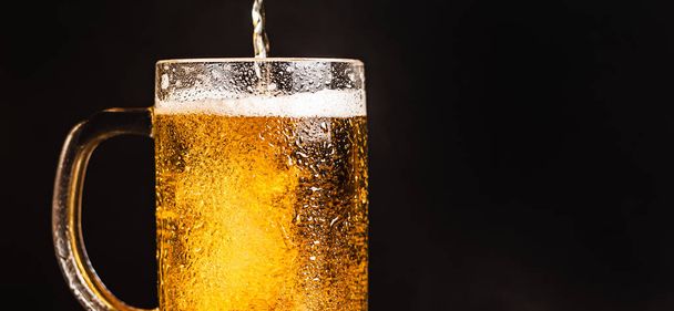 Cold beer with foam in a mug, on a wooden table and a dark background with