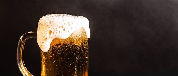 Cerveja fria com espuma em uma caneca, em uma mesa de madeira e um fundo escuro com espaço em branco para um logotipo ou texto. Foto caneca de estoque de cerveja espumosa fria close-up
. - Foto, Imagem