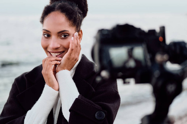 Красивая милая афроамериканка счастливо позирует перед камерой во время фотосессии у моря
 - Фото, изображение