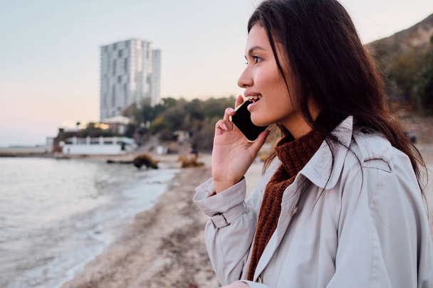 Widok z boku wesoły Azji brunetka dziewczyna szczęśliwie rozmawiać przez telefon komórkowy na plaży miasta - Zdjęcie, obraz