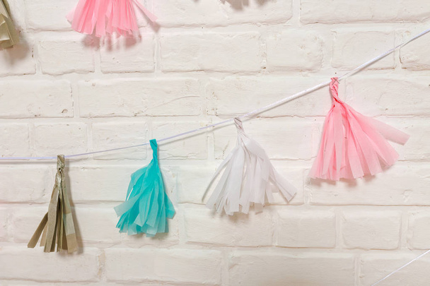 Multicolored paper garlands on a white brick wall.  Tissue paper tassels Garlands bunting happy birthday wedding party decor. Blue and pink paper garlands for kids birthday party - Photo, Image