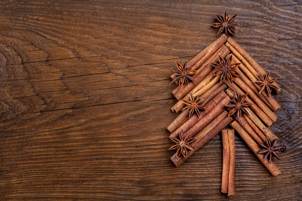 スパイスシナモンスティック、素朴な木製の背景にアニススターから作られたモミの木でクリスマスカード。お祝いのコンセプト。テキスト、フラットレイアウト、トップビュー、コピースペースのための場所 - 写真・画像