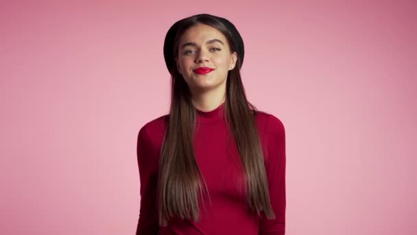 Young hipster woman with red lips and hat making thumbs up sign over pink background. Winner. Success. Positive girl smiles to camera. Body language. Slow motion. - Materiaali, video