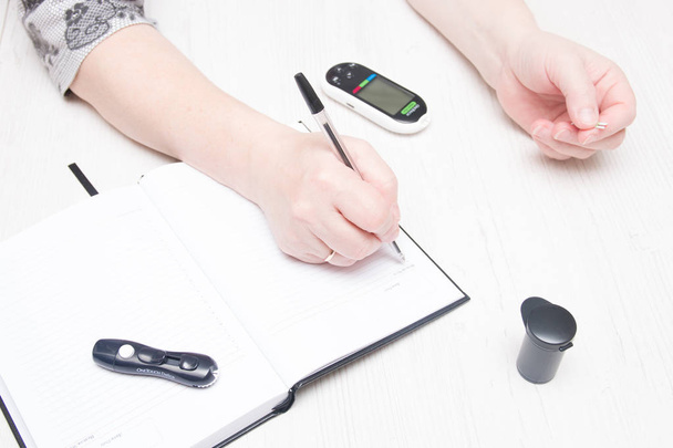 woman writes the result of a blood test for sugar in a notebook, diabetes control, glucose meter concept - Foto, imagen
