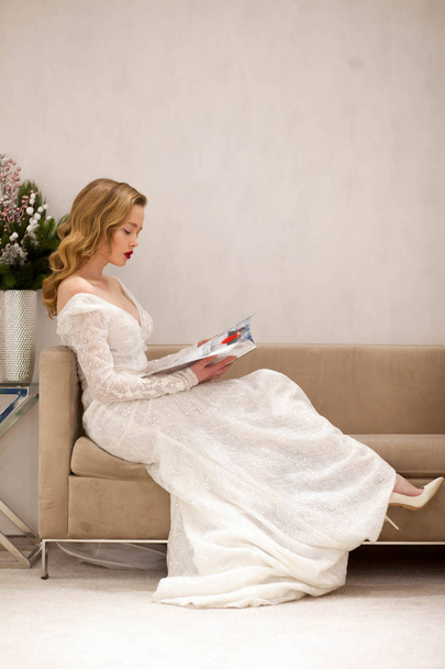 A menina em um vestido bonito olha diário no sofá
 - Foto, Imagem