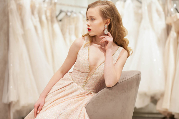 Nevěsta v elegantních šatech pózuje na židli ve svatebním salonu - Fotografie, Obrázek